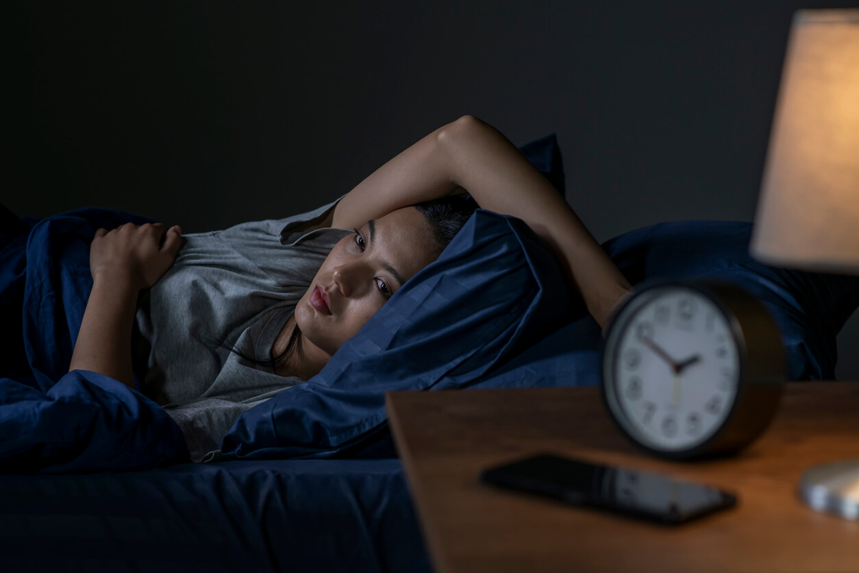 Mulher deitada na cama, com dificuldade para dormir e expressão de cansaço, ilustrando a relação entre intestino e sono.