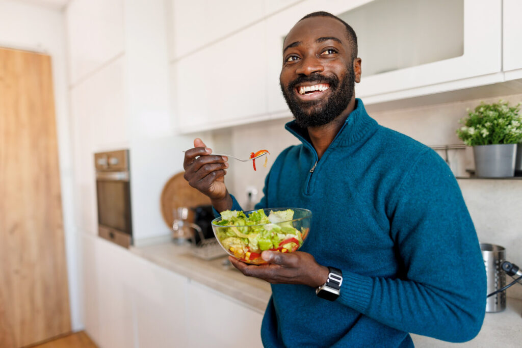 Homem sorridente segurando tigela de salada colorida, representando escolhas alimentares que favorecem a absorção de nutrientes e o bem-estar.