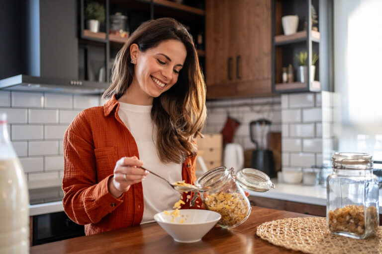 Mulher sorridente preparando uma tigela de cereal rico em fibras, destacando a importância dos alimentos ricos em fibras para a saúde intestinal.