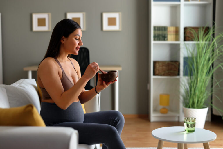 Mulher grávida sentada no sofá faz refeição saudável, representando a importância do consumo de probióticos para gestantes no apoio à saúde intestinal e imunidade