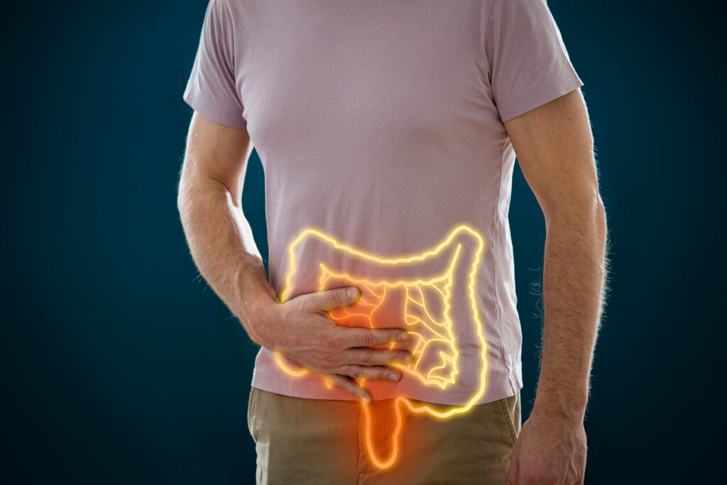 Flora intestinal: o que é e como manter saudável jejum intermitente Homem com a mão na região abdominal e ilustração do intestino sobreposta, representando o equilíbrio da flora intestinal e a saúde digestiva.
