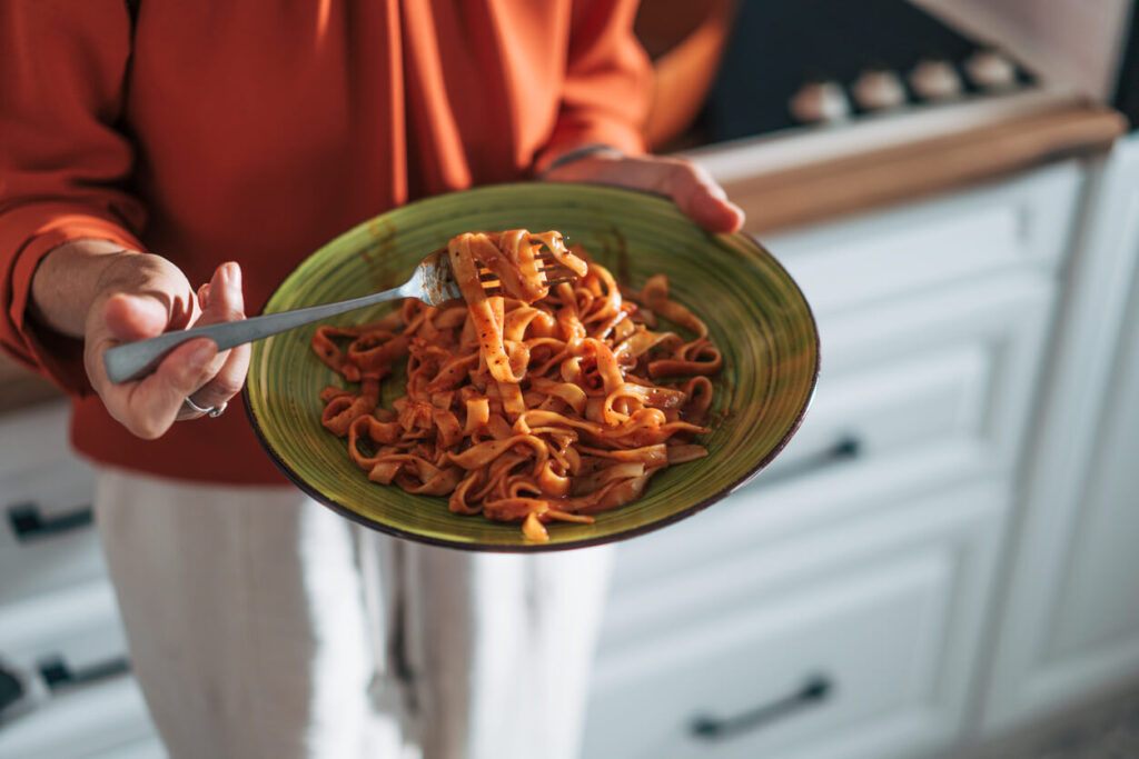 O que são carboidratos e por que escolher os certos faz diferença jejum intermitente Pessoa segurando prato de macarrão com molho, representando alimentos ricos em carboidratos e a importância de fazer escolhas equilibradas.