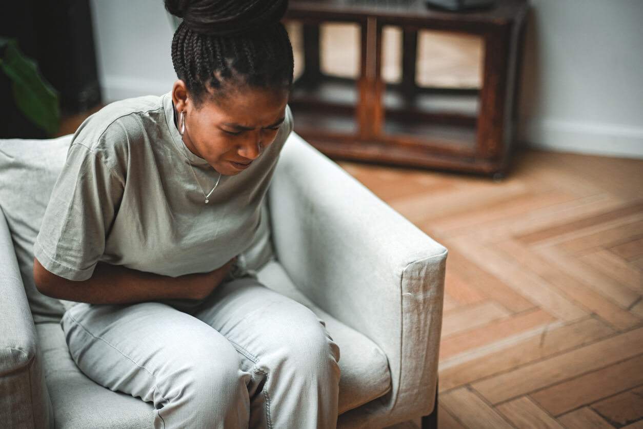 Mulher sentada com dor abdominal, representando os sinais de alerta da diarreia em adultos e a importância de buscar orientação médica.